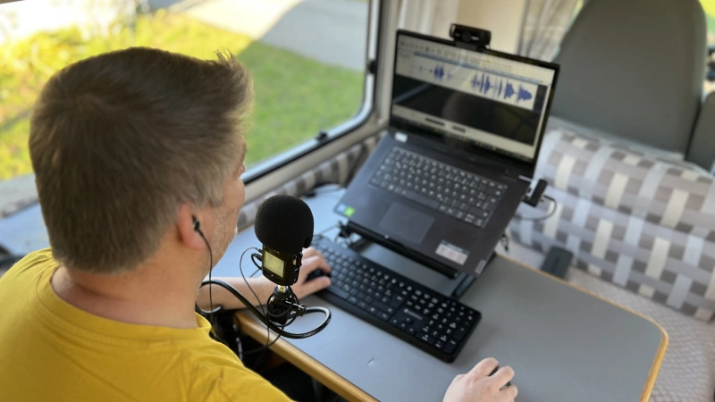 andre-christen-podcast-moderator André Christen führt ein Podcast-Interview mit Mikrofon und Laptop im Camper – strukturierte Gespräche mit Wirkung